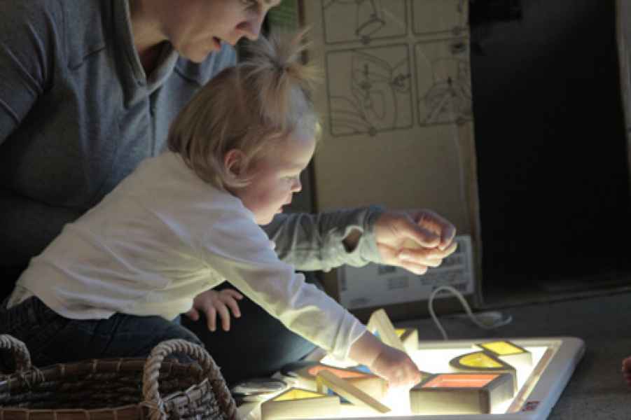 infant and educator playing with shapes at a light table
